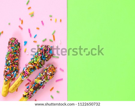 biscuit stick chocolate topping with rainbow sugar on pink and green background in copy space