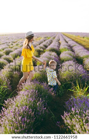 Young woman in yellow dress walk on purple lavender flower meadow field background, rest, have fun, play with little cute child baby boy. Mother, small kid son. Family day, parents, children concept