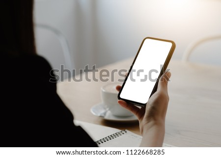 Mockup image of a woman holding mobile phone with blank black screen in modern loft cafe
