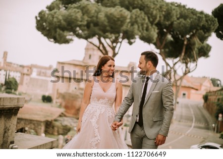 Young attractive newly married couple walking and posing in Rome with beautiful and ancient architecture on the background on their wedding day