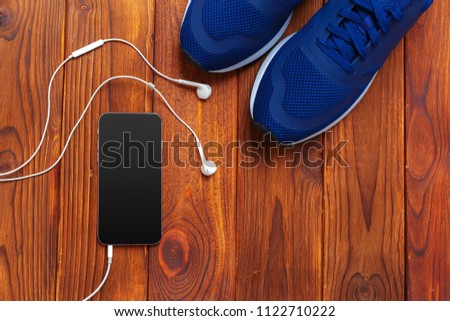 Sneakers and mobile phone with headphones on wooden table