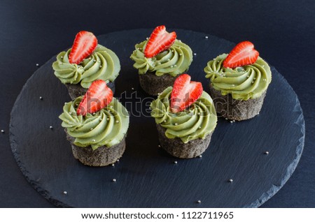 Black cupcakes with green cream and fresh strawberry on black background