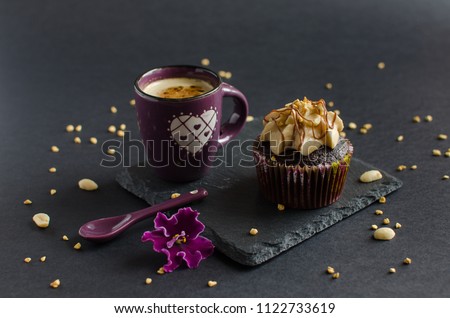 Cup of coffee and chocolate cupcake with walnut cream, chocolate sauce and peanut on black board, decorated with purple flower