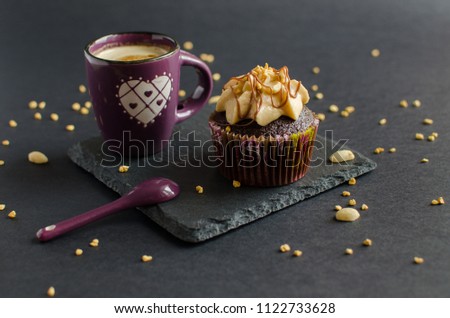 Cup of coffee and chocolate cupcake with walnut cream, chocolate sauce and peanut on black board
