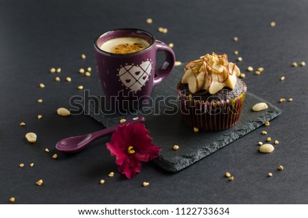 Cup of coffee and chocolate cupcake with walnut cream, chocolate sauce and peanut on black board, decorated with red flower