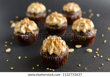 Chocolate cupcakes with walnut cream, chocolate sauce and peanut on black background