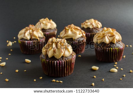 Chocolate cupcakes with walnut cream, chocolate sauce and peanut on black background
