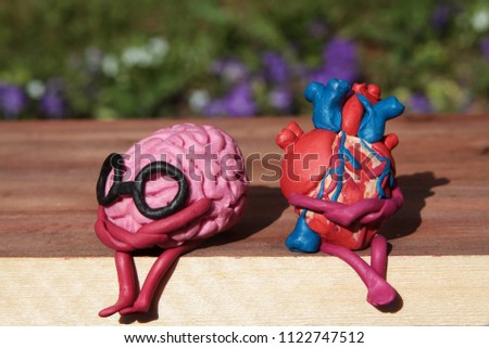 Plasticine human heart and brain are sitting on a wooden bench in the park. Disharmonious unhappy person concept