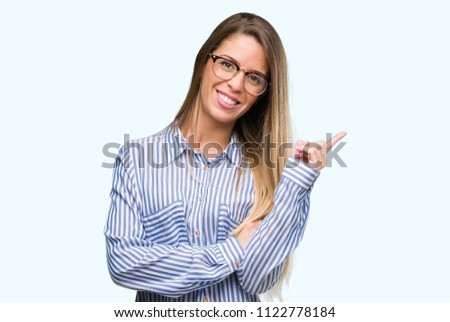 Beautiful young woman wearing elegant shirt and glasses with a big smile on face, pointing with hand and finger to the side looking at the camera.