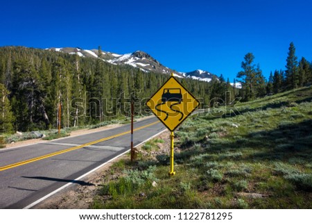 Yellow "slippery road" sign with snowy forest peaks - Highway 108 Roadside, California