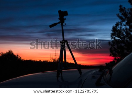 Closeup of mirrorless camera and tripod on the hood of a car during a colorful Tahoe forest sunset.