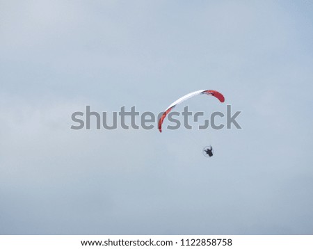 Paraglider in a red and white wing gliding in the Dutch Spring sky over Zwolle - Overijssel Region on a cloudy day