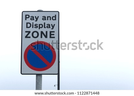 Pay and Display Zone sign with black text on white background with red circle on blue background against a clear white sky.