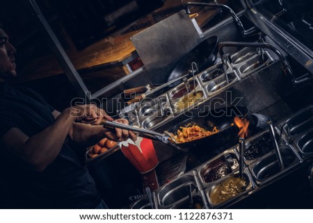 Cooking process in an Asian restaurant. Cook is stirring vegetables in wok. 