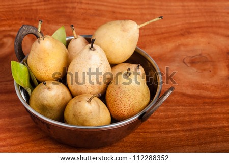 Photo of yellow pears in a copper bowl on a wooden table