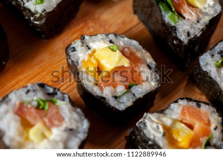 Close up of pieces of home made colourful Sushi with rice, mango, salmon on a wooden plate