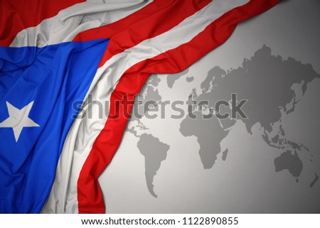 waving colorful national flag of puerto rico on a gray world map background.