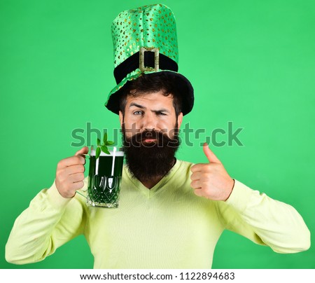 St Patrick's Day. Serious man holds glass of beer on St.Patrick's day. Saint Patrick's Day concept - bearded man in leprechaun hat shows thumbs up pours beer. St Patrick's Day green beer with shamrock Royalty-Free Stock Photo #1122894683