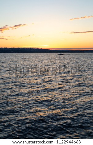 Lake sunset scene with a motorboat cruising on dark blue and purple water, with a colorful sunset on the horizon 