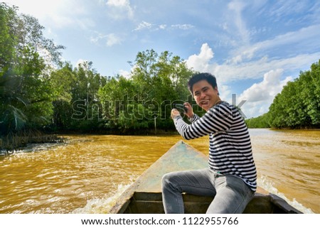 Happy black and white shirt Male Traveler uses camera for taking the beautiful sky and natural view photo while sailing on the boat along the rive to visit nature  Mangrove Ecosystem environment