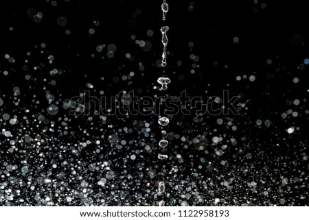 A stream of water dropping from above and splashing into a large amount of water droplets against a black background