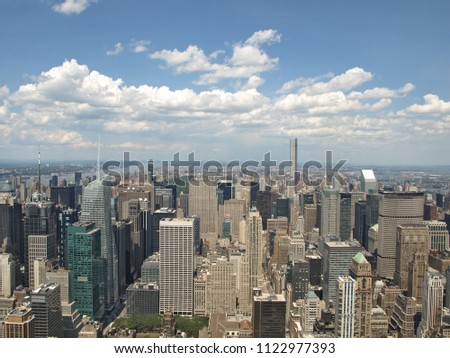 A panoramic view of skyscrapers and buildings towering over the city below on a clear, bright day with the sky off in the distance.