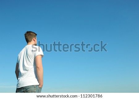 Young man in white t-shirt standing in front of blue sky. On the right side space for text or graphics.