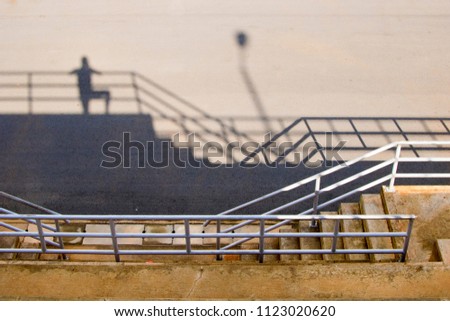 shadow of a person standing on the top of some stairs near the railings at a sporting facility watching a game. shadow of a photographer on the ground
