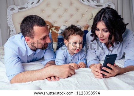 happy family beautiful mother little son and father watching cartoon in phone lying on bed in bedroom