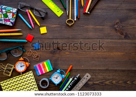 Student accessories. Stationery mockup with glasses, alarm clock, notebook on dark wooden background top view copy space