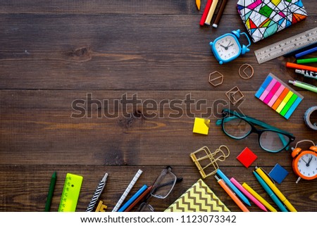 Student accessories. Stationery mockup with glasses, alarm clock, notebook on dark wooden background top view space for text