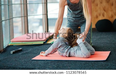 A little girl repeats exercises for her mother in the gym