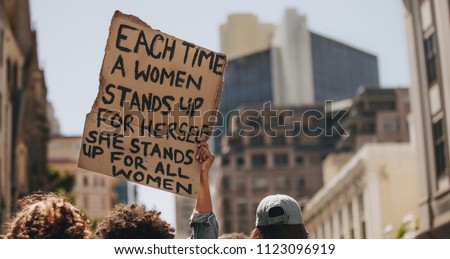 Group of demonstrators on road with a signboard saying each time a woman stands up for herself she stands up for all women. Activist demonstrating women power.