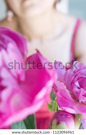 a bouquet of pink peonies with green branches in the morning light in the hands of a woman without a face on the background of a pink dress