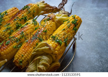Native American cuisine, roasted corncobs with green herbs and sauce on blue marble background, close-up. Grilled corn, healthy eating concept. Selective Focus