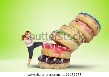 Picture of fat woman refusing to eat sweet food by kicking a pile of donuts. Shot with green screen background
