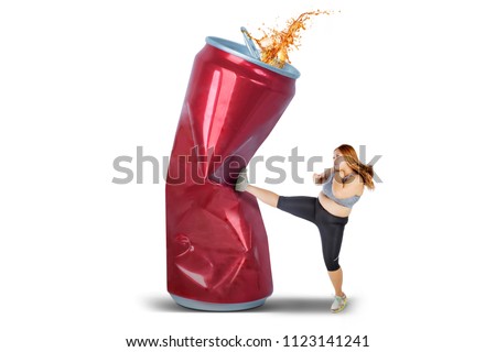 Picture of beautiful fat woman kicking a can of soft drink, isolated on white background