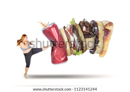 Picture of beautiful fat woman wearing sportswear while kicking soft drink and fast food, isolated on white background