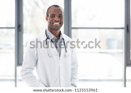 Sincere smile. Handsome practitioner keeping smile on face and looking straight at camera Royalty-Free Stock Photo #1123153961