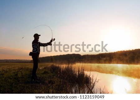 Silhouette of a fisherman at dawn to fish in the river. A cold summer morning and mist over the water.