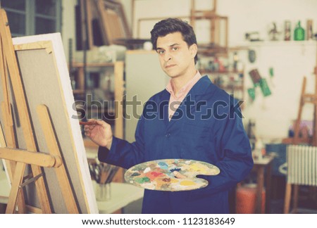 Smiling man with brush near easel painting on canvas