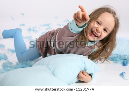 Five years old girl having fun with blue pillows and feathers on white background. Pillow fight !