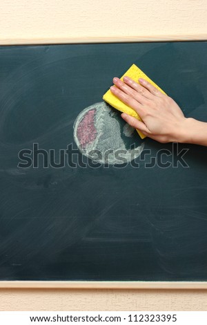 hand with a yellow sponge cleaning the chalkboard