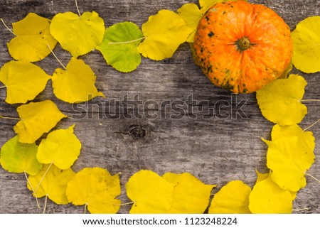 Frame of autumn yellow leaves and pumpkin on rustic wooden background. Top view, copy space