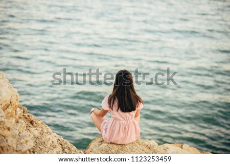 Beautiful girl sitting on a rock and looking to the sea. Soft focus.