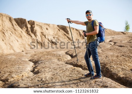 Image of athlete man with backpack and walking sticks pointing with hand to side