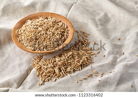 Oat groats or oat spike in wooden plate on homespun tablecloth background, copy space, top view, selective focus