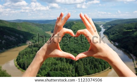 Hands heart gesture against panoramic summer view of the Saar river bend in Saarland, Germany. Saarschleife loop from the lookout point Cloef.

 Royalty-Free Stock Photo #1123374506