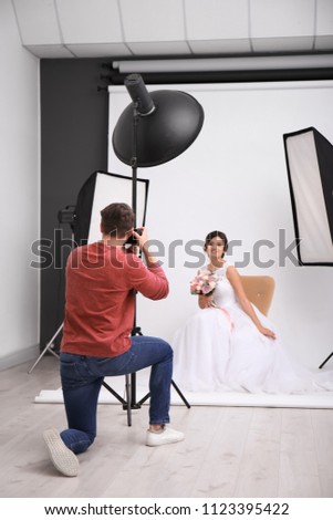 Professional photographer taking photo of beautiful bride in studio