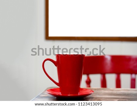 Red mug coffee on wooden table with picture frame on wooden wall and blurry background of red chair, Cropped image of poster mock up template with red cup on wooden table over blurry white wall